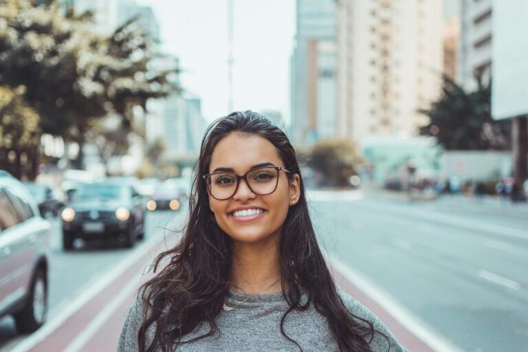 Team A young woman with glasses smiling on a city street, embracing urban lifestyle.